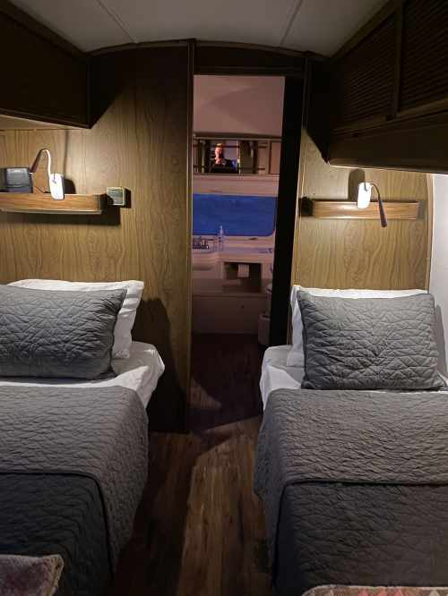 A cozy cabin with two twin beds, wooden walls, and a view of the ocean through an open door.