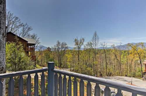 View from a balcony overlooking a forested area with mountains in the distance under a clear blue sky.