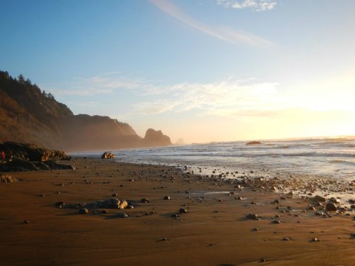 A serene beach at sunset, with gentle waves, rocky cliffs, and a clear sky.