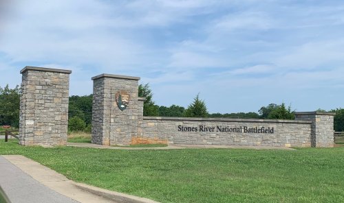 Stone entrance sign for Stones River National Battlefield, surrounded by green grass and trees under a blue sky.