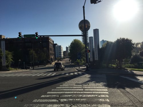 A sunny street view with traffic lights, a crosswalk, and a large spherical structure in the background.