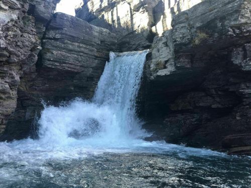 A waterfall cascading over rocky cliffs into a pool of water below, surrounded by rugged stone formations.