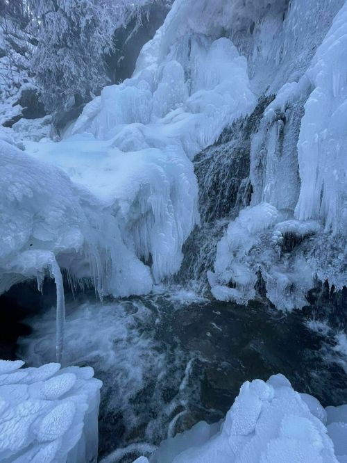 A frozen waterfall surrounded by ice formations and a flowing stream, creating a serene winter landscape.