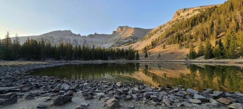 A serene mountain lake reflecting surrounding trees and rocky terrain under a clear blue sky.