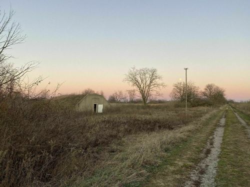 A dirt path leads through tall grass to a small, abandoned structure under a pastel sky at dusk.
