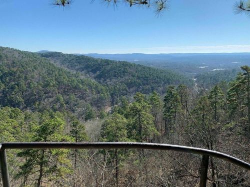 A scenic view from a lookout point, showcasing lush green mountains and a clear blue sky.
