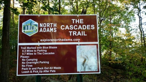 Sign for North Adams' Cascades Trail, detailing distance to trailhead and rules for visitors. Surrounded by trees.