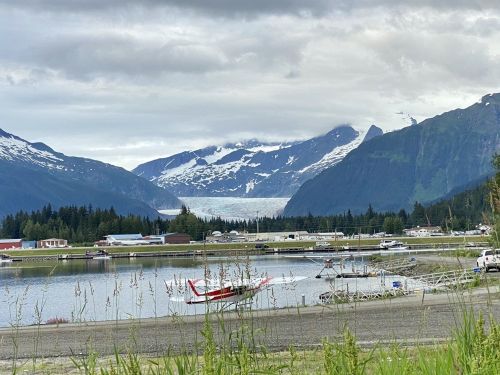 A scenic view of a glacier between mountains, with a calm lake and small boats in the foreground.