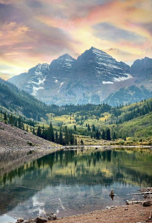 A serene mountain landscape with a reflective lake, surrounded by lush trees and colorful skies at sunset.