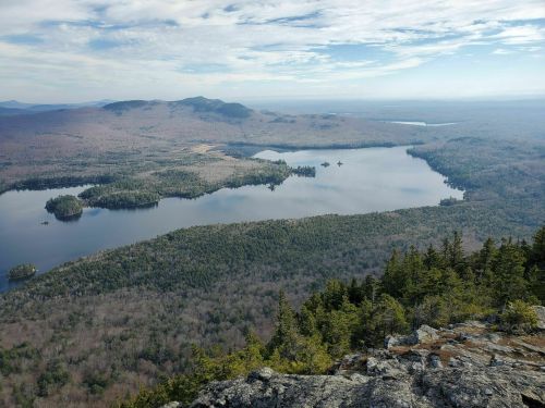 A panoramic view of a serene lake surrounded by forested hills under a clear sky.