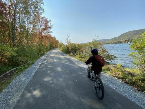 A person rides a bicycle along a scenic path by a lake, surrounded by colorful autumn foliage.
