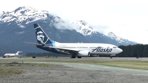 An Alaska Airlines plane taxiing on a runway with snow-capped mountains in the background.
