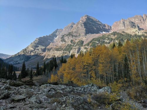 A scenic mountain landscape with autumn foliage, featuring rocky terrain and tall peaks under a clear blue sky.
