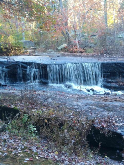 A serene waterfall cascading over rocks, surrounded by autumn foliage and trees in a peaceful natural setting.