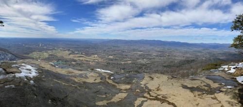 A panoramic view of rolling hills and valleys under a blue sky with scattered clouds, seen from a rocky overlook.