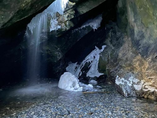 A dark cave with icicles hanging from the ceiling, a small waterfall, and a rocky, icy floor.