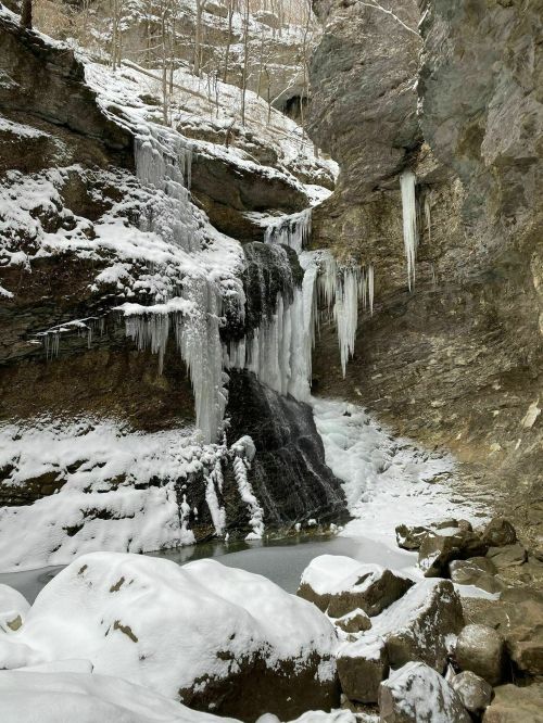 A frozen waterfall surrounded by snow-covered rocks and icicles, set in a rocky canyon.