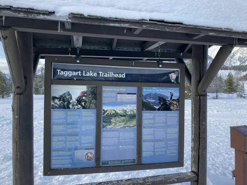 Sign at Taggart Lake Trailhead with information about the trail and safety in the backcountry, surrounded by snow.