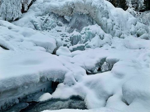 A winter landscape featuring a frozen river and snow-covered rocks, with icy formations and a serene, white atmosphere.