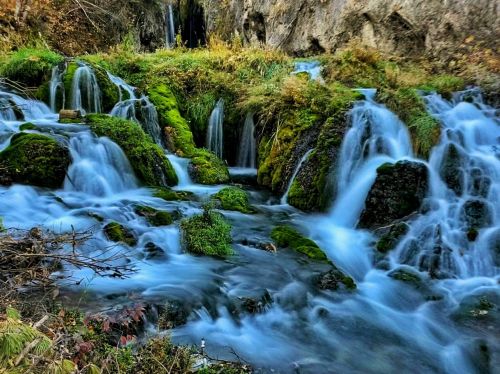 A serene landscape featuring cascading waterfalls over moss-covered rocks, surrounded by lush greenery.