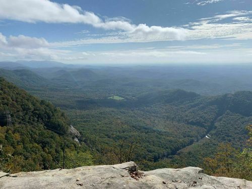 A panoramic view of rolling green mountains under a partly cloudy sky, with a valley visible in the distance.