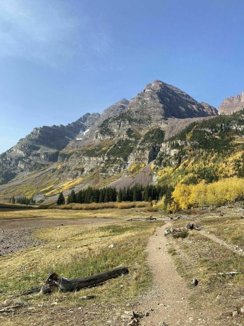 A scenic mountain landscape with autumn foliage, a dirt path, and clear blue skies.