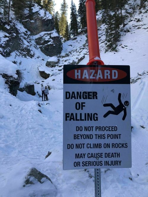 Sign warning of falling hazards in a snowy area, advising against proceeding and climbing on rocks.
