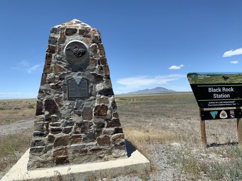 Stone monument with plaques, next to a sign for Black Rock Station, set against a vast, open landscape and blue sky.