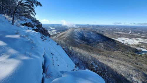 A snowy mountain landscape with a clear blue sky and distant hills, showcasing a serene winter scene.