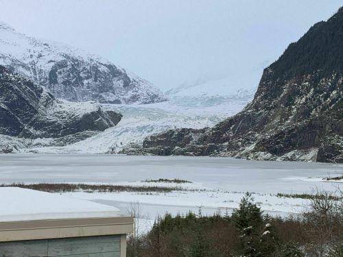 A snowy landscape featuring a glacier between mountains, with a frozen lake in the foreground.