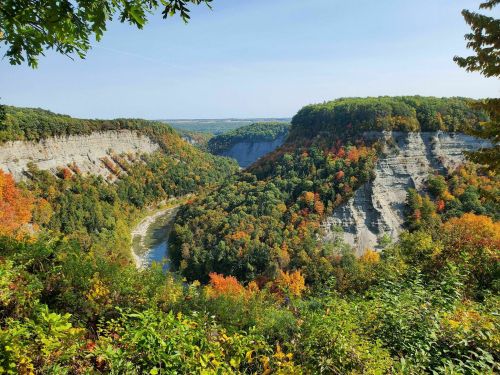 A scenic view of a river valley surrounded by colorful autumn foliage and steep cliffs under a clear blue sky.