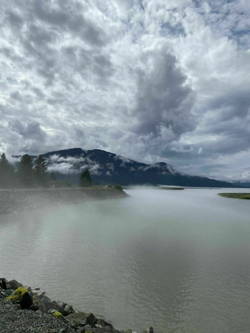 A serene landscape featuring a misty river, mountains in the background, and a cloudy sky.