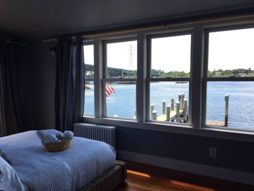 A cozy bedroom with a view of a river and a bridge, featuring a basket on the bed and an American flag outside.