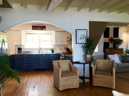 Bright, airy kitchen with blue cabinets, wooden floors, and cozy seating area featuring woven chairs and plants.