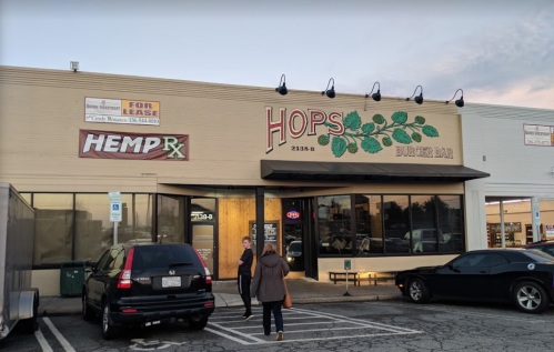 Exterior of Hops Burger Bar with a "For Lease" sign, parked cars, and people walking in front.