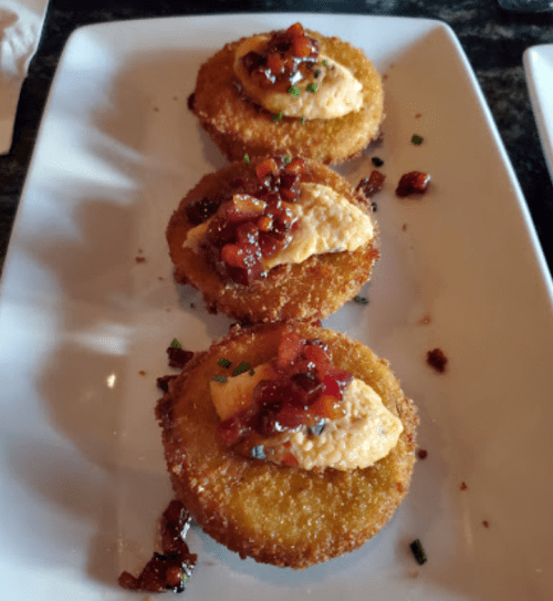 Three golden fried cakes topped with creamy spread and a sweet red sauce, served on a white plate.
