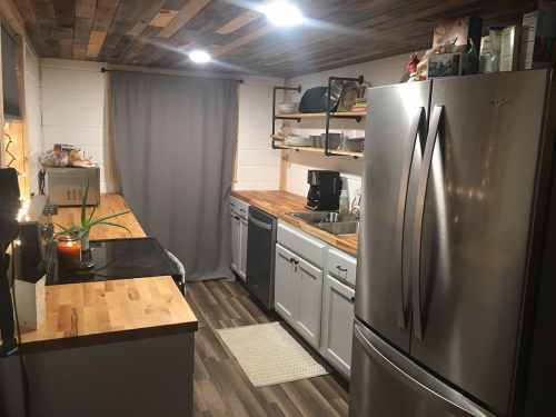 A modern kitchen with wooden countertops, stainless steel appliances, and a cozy atmosphere, featuring a curtain and shelves.