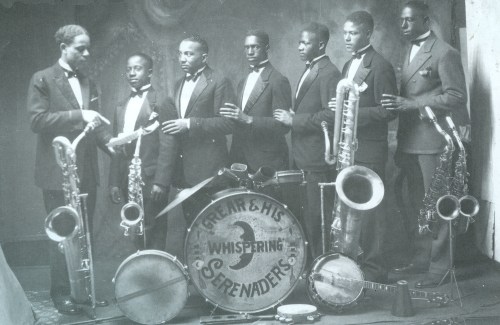 A vintage photo of a jazz band, featuring seven musicians with various instruments, dressed in formal attire.