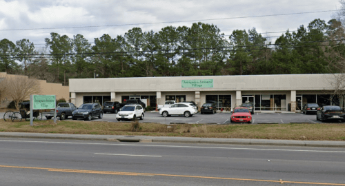 A row of shops with a sign reading "Antiques & Artisan Village," surrounded by trees and parked cars.