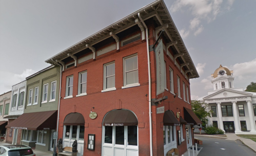 Historic brick building with awnings, next to a clock tower and courthouse, under a cloudy sky.
