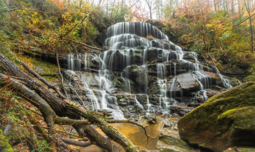 A serene waterfall cascades over rocky cliffs, surrounded by autumn foliage and a tranquil pool below.