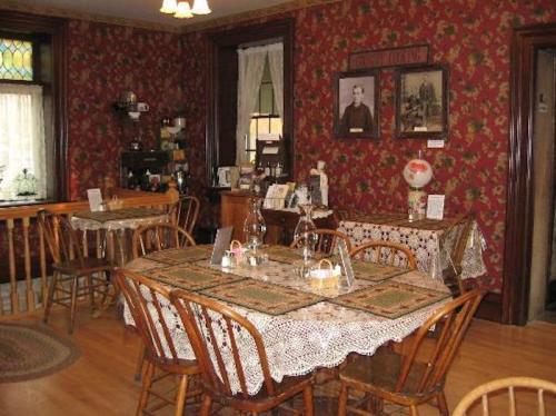 Cozy dining room with floral wallpaper, wooden tables, lace tablecloths, and vintage decor.