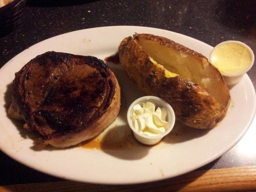 A plate with a grilled steak, a baked potato with butter, and a small cup of sour cream.