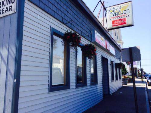 Exterior of Chez Vachon restaurant, featuring a sign, flower baskets, and large windows on a sunny day.