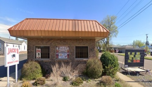 A small brick building with a metal roof, featuring signs for Jack's restaurant and a takeout order notice.
