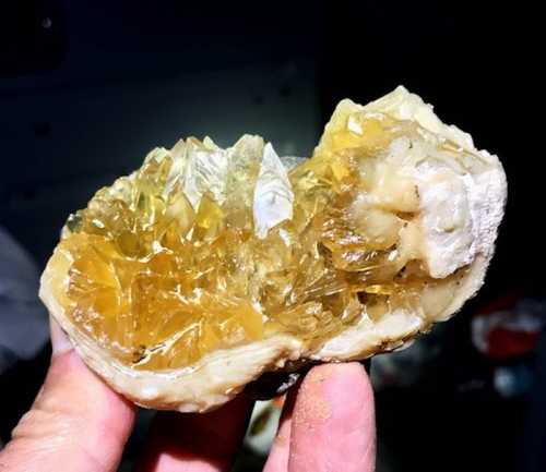 A hand holding a large, translucent yellow crystal cluster embedded in a rock.