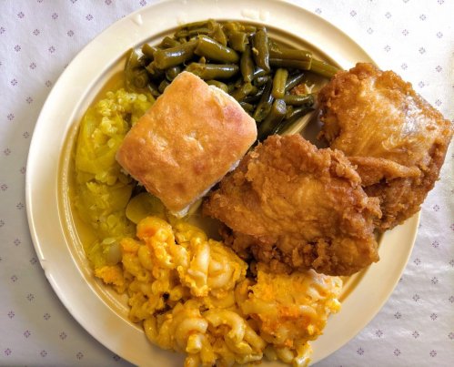 A plate of fried chicken, macaroni and cheese, green beans, pickled vegetables, and a biscuit.