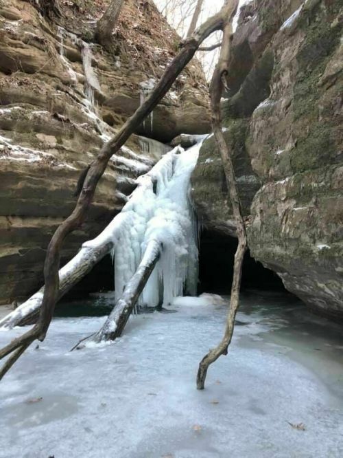 A frozen waterfall surrounded by icy rocks and bare trees in a winter landscape.