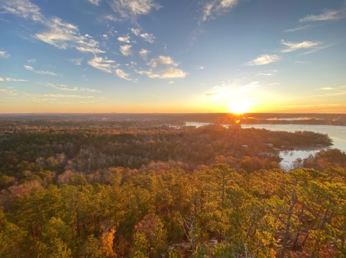 A scenic view of a sunset over a forested landscape and a lake, with vibrant colors in the sky.