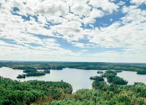 A scenic view of a lake surrounded by lush green forests and islands, under a partly cloudy sky.